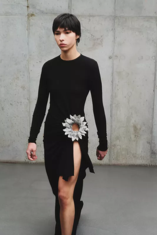 Обтягивающее черное платье с разрезом и декоративным цветком, акцентирующим внимание на талии и создающим эффектный образ