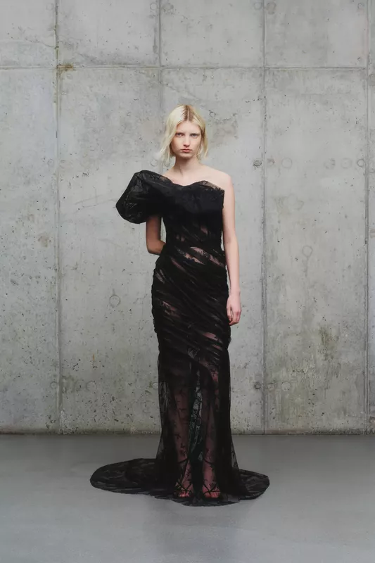 Платье с асимметричным рукавом и прозрачной текстурой, создающее эффект легкости и изысканности на фоне серого бетона