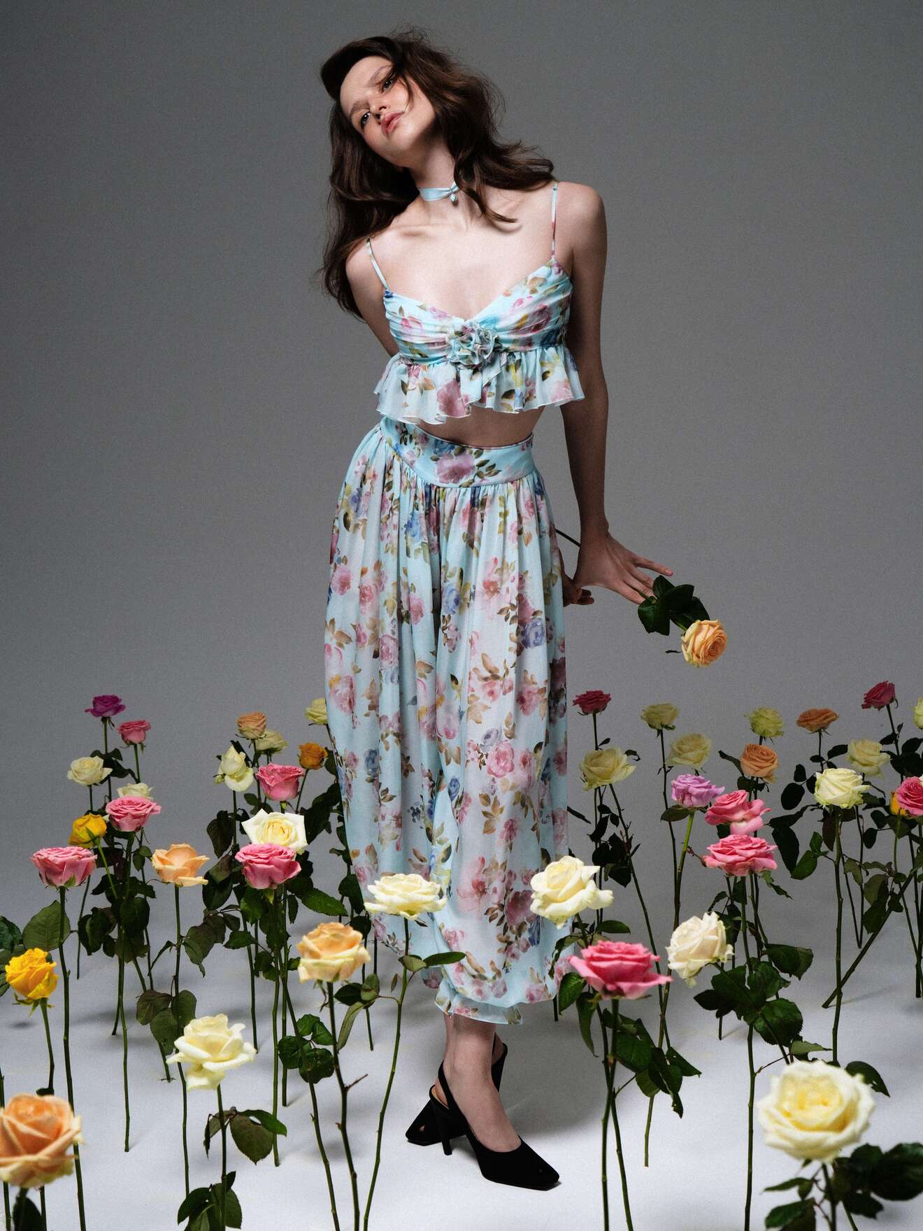 Нежный комплект из топа и юбки с цветочным узором, создающий игривый образ на фоне цветущих роз