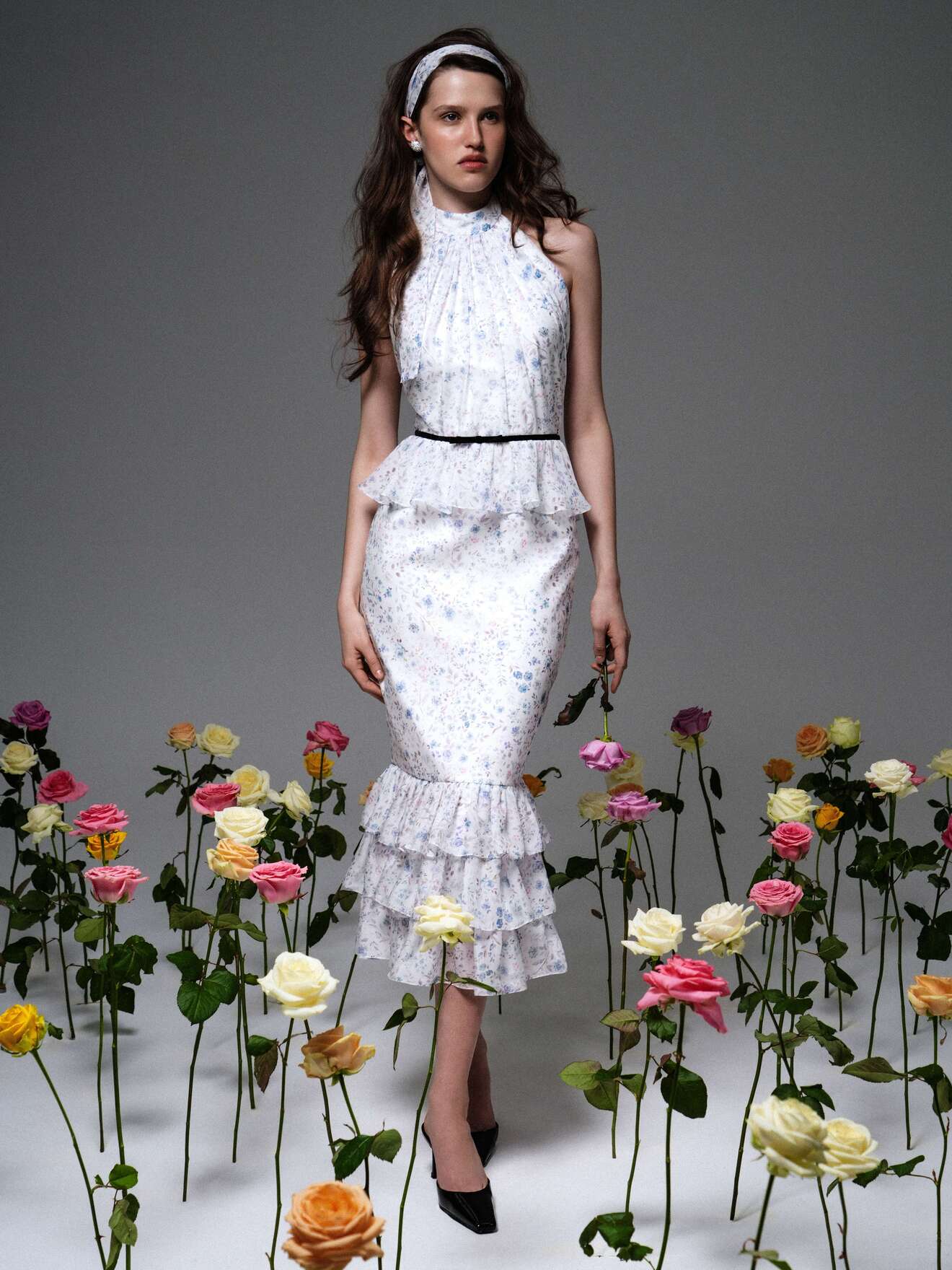 Стильное платье с пышной юбкой и черным поясом, дополненное головным убором, среди ярких розовых и желтых цветов