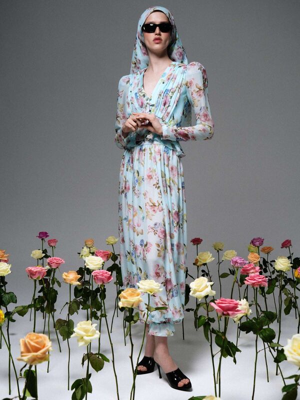 Элегантное платье с длинными рукавами и головным убором, дополненное солнцезащитными очками, в окружении розовых цветов