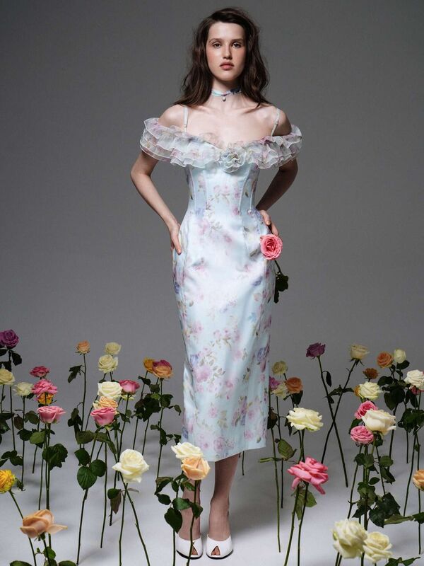 Нежное платье с цветочным принтом, рюшами и открытыми плечами, окруженное яркими розами в весенней атмосфере
