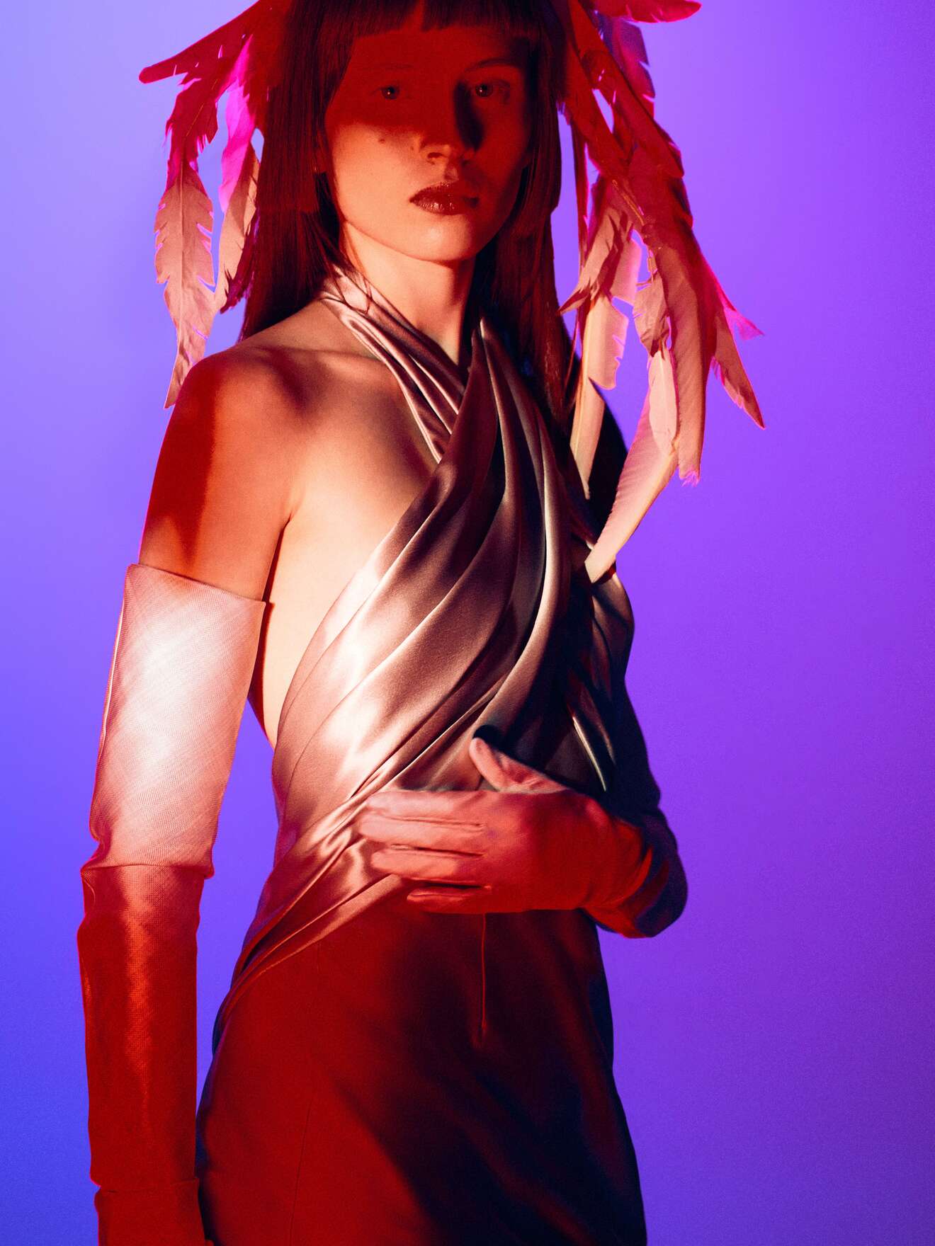 Обтягивающее платье с драпировкой и перьями, освещенное яркими красными и фиолетовыми тонами, создающими загадочную атмосферу