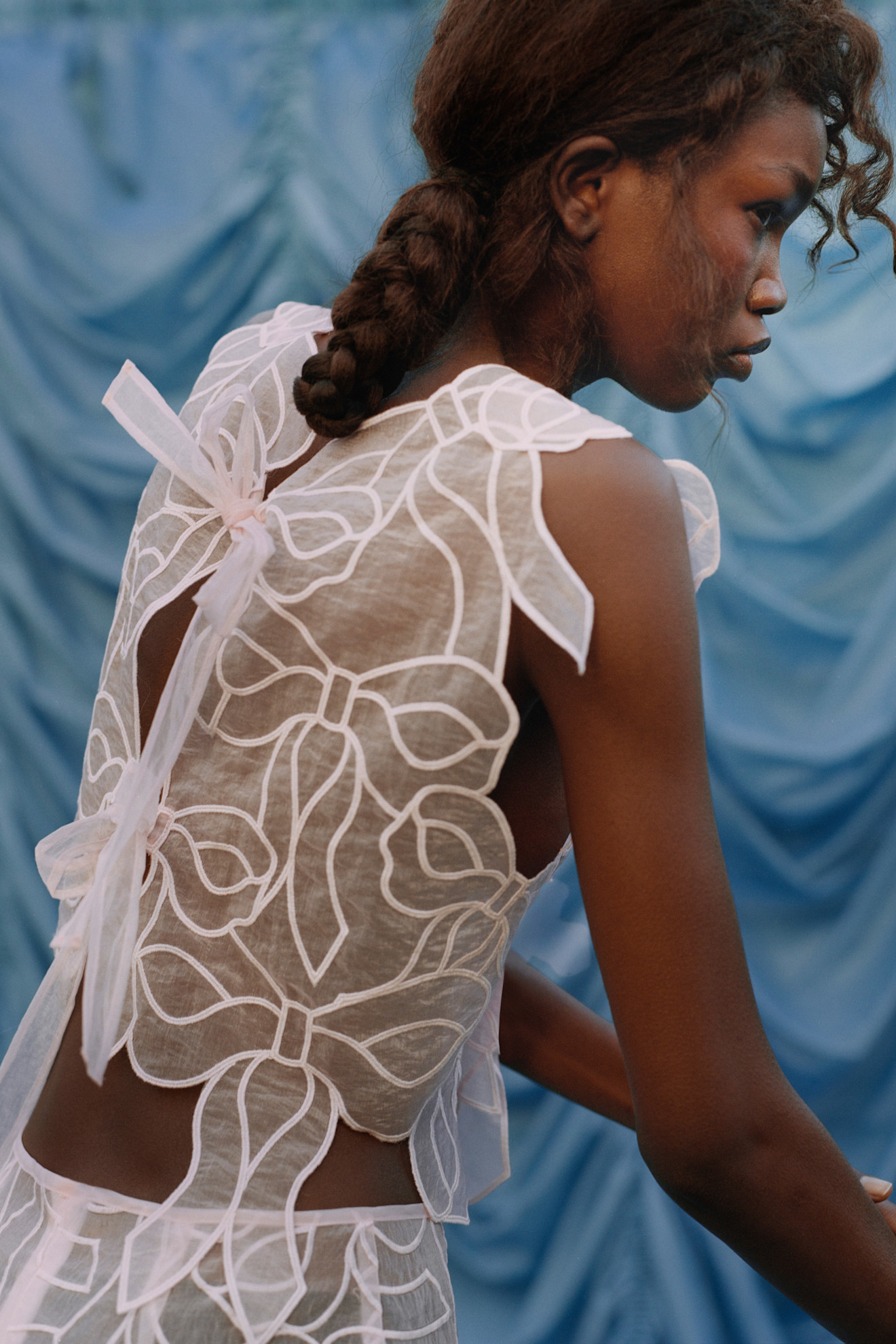 Тонкая блуза с объемными рюшами и нежными бантами, создающая романтичный образ на фоне голубого текстиля