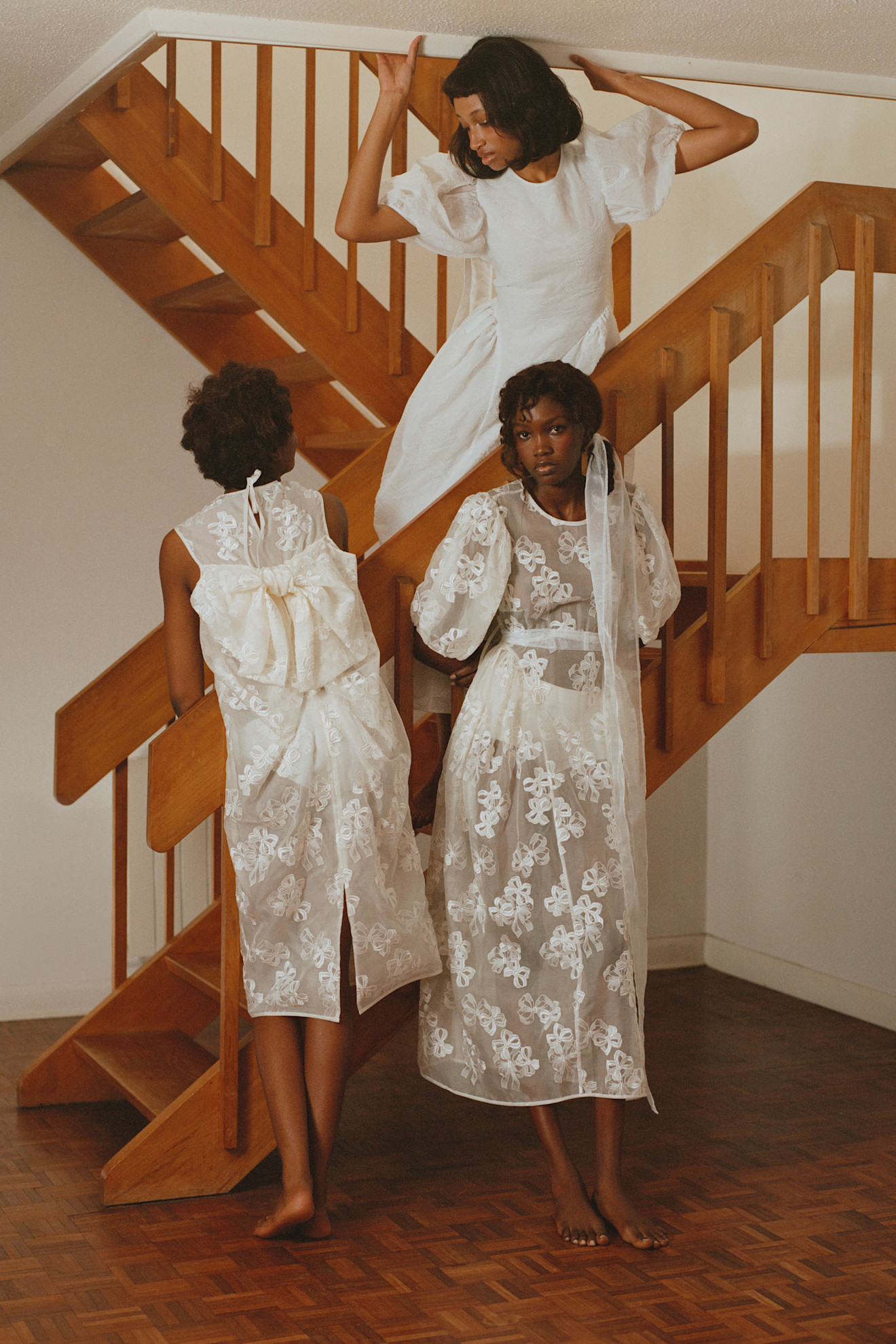 Три девушки в воздушных белых и прозрачных платьях с вышивкой, позирующие на лестнице, создают атмосферу легкости