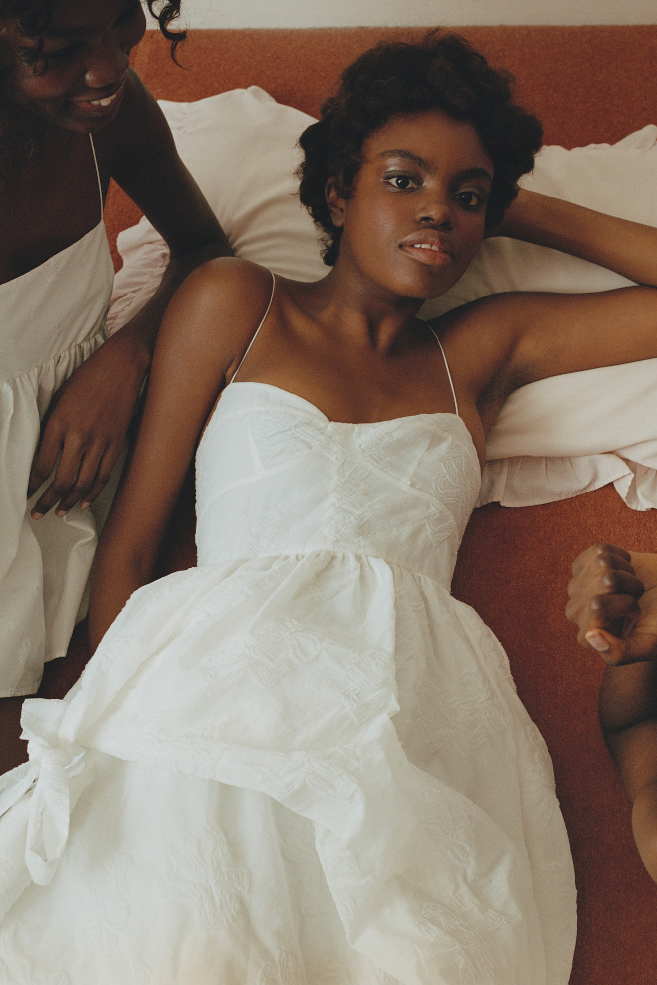 Легкое белое платье с рюшами и тонкими бретелями, создающее атмосферу нежности и уюта на фоне теплых тонов интерьера