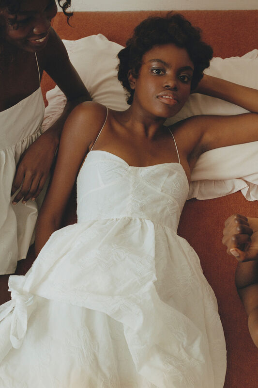 Легкое белое платье с рюшами и тонкими бретелями, создающее атмосферу нежности и уюта на фоне теплых тонов интерьера