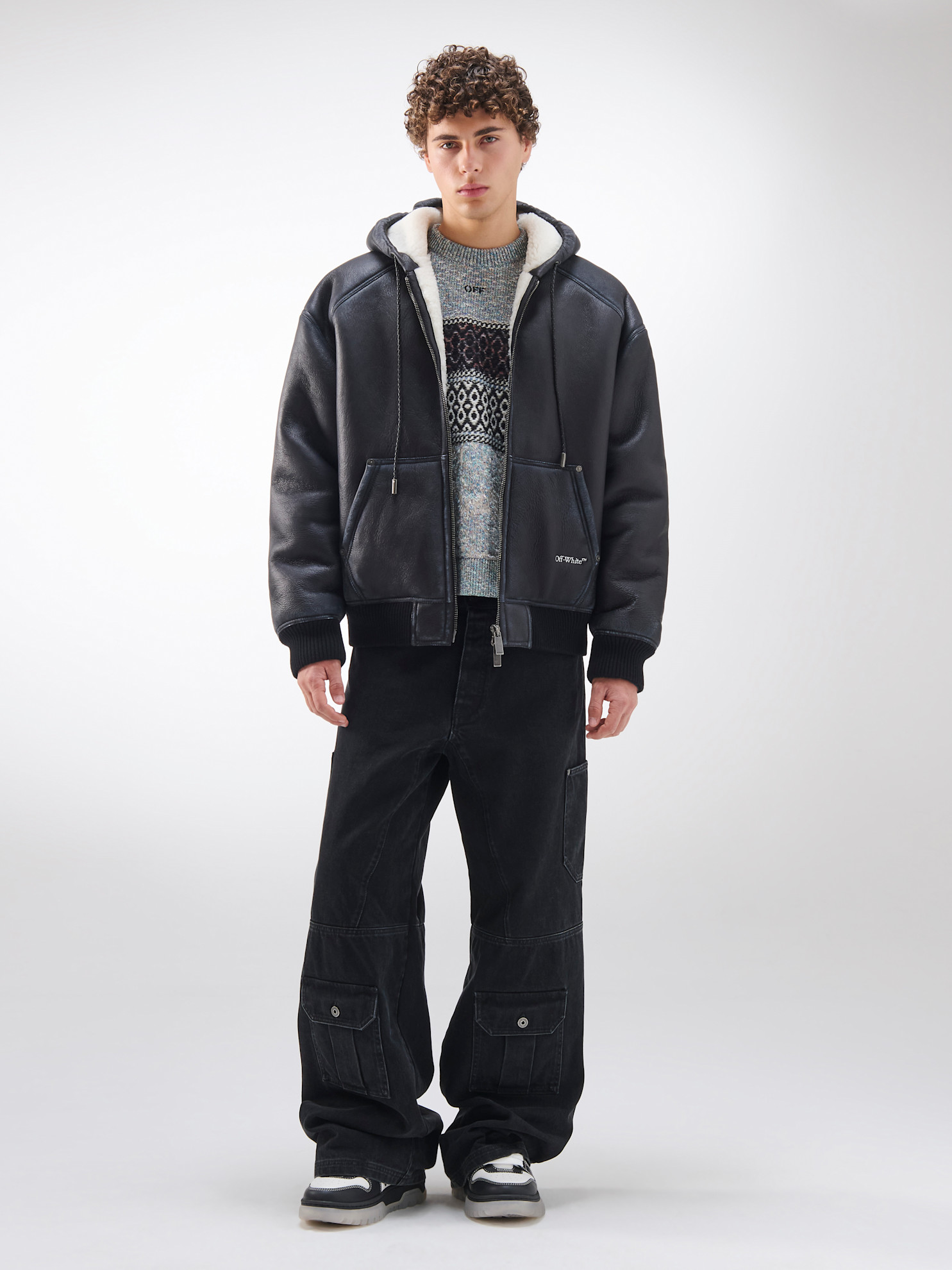 Кожаная куртка с меховой подкладкой в сочетании с ярким свитером и широкими черными брюками, создающими эффектный силуэт