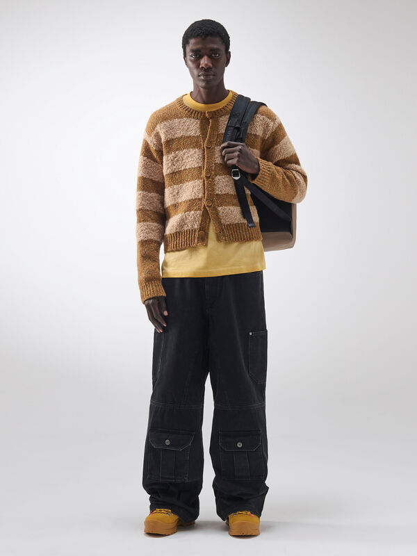 Стильный вязаный кардиган в полоску, надетый на желтую футболку и черные брюки, придает образу уют и оригинальность