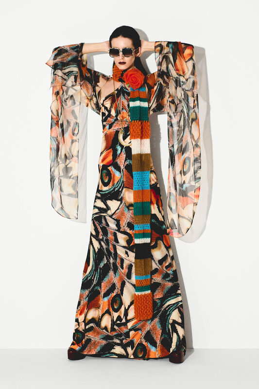 Платье с объемными рукавами и ярким принтом, дополненное длинным шарфом и стильными очками, создающими эффектный силуэт