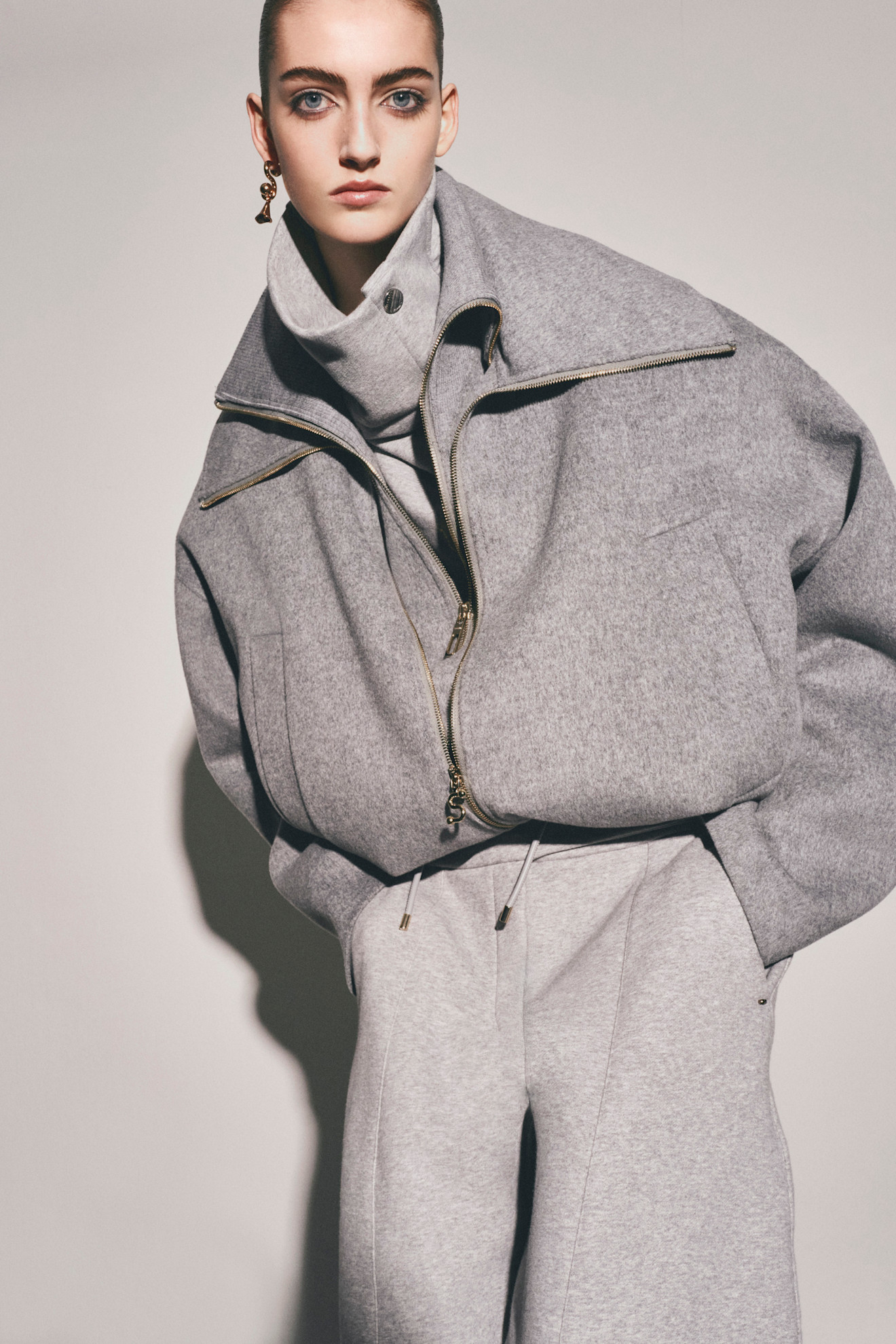 Серый спортивный костюм с объемной курткой и высоким воротником, дополненный золотыми деталями