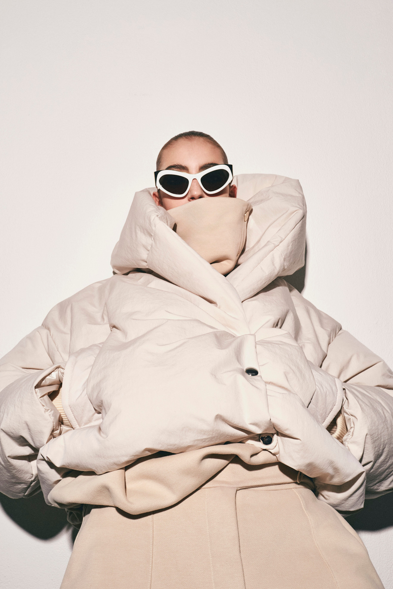 Крупный пуховик и аксессуары в нейтральных тонах, акцентируют внимание на выразительном лице модели