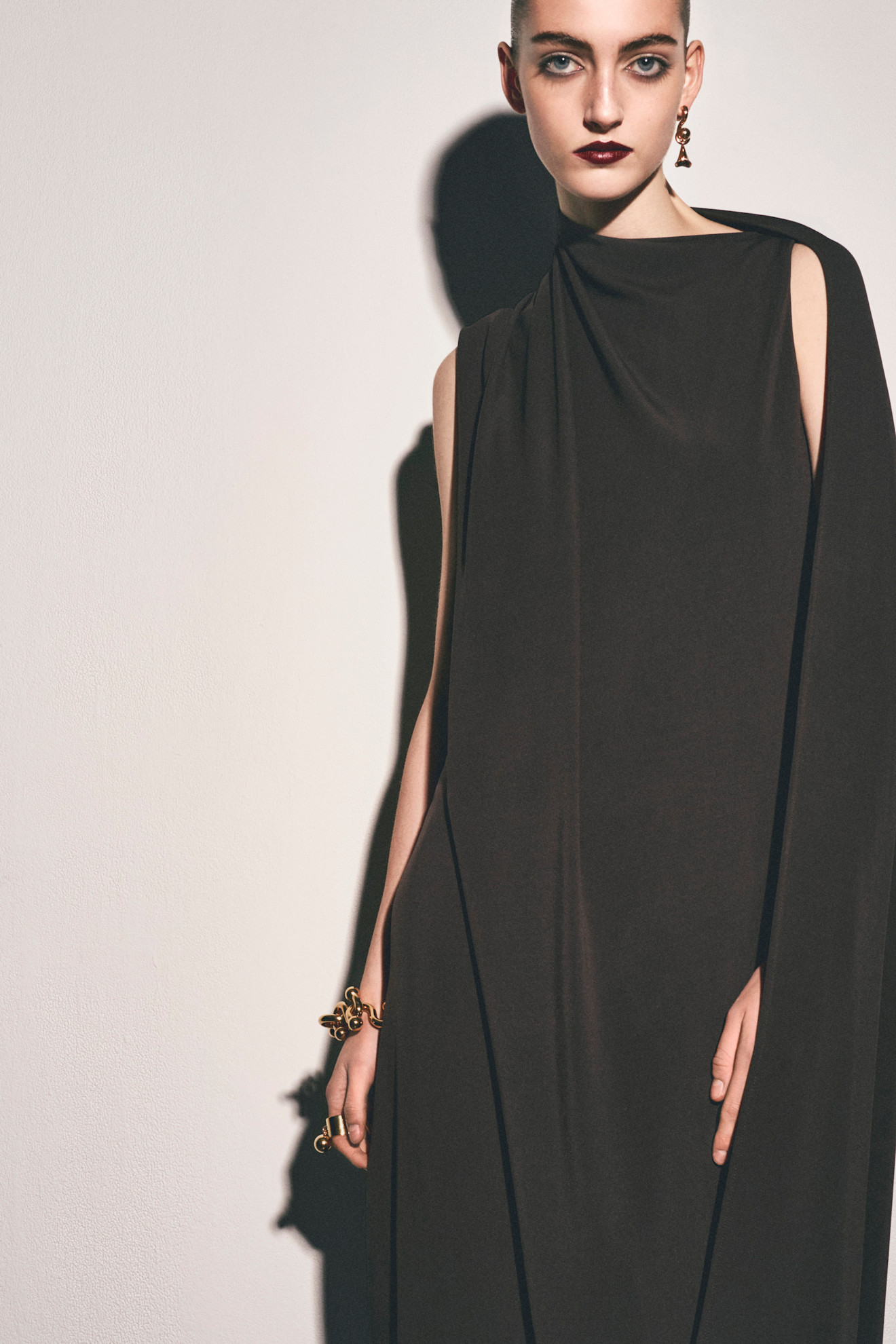 Минималистичное темно-коричневое платье с драпировкой, акцент на выразительные серьги и глубокий макияж