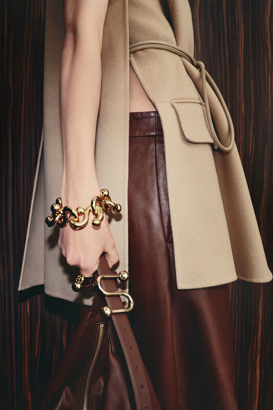 Нежный бежевый жилет с поясом и коричневыми кожаными брюками, дополненный массивным золотым браслетом