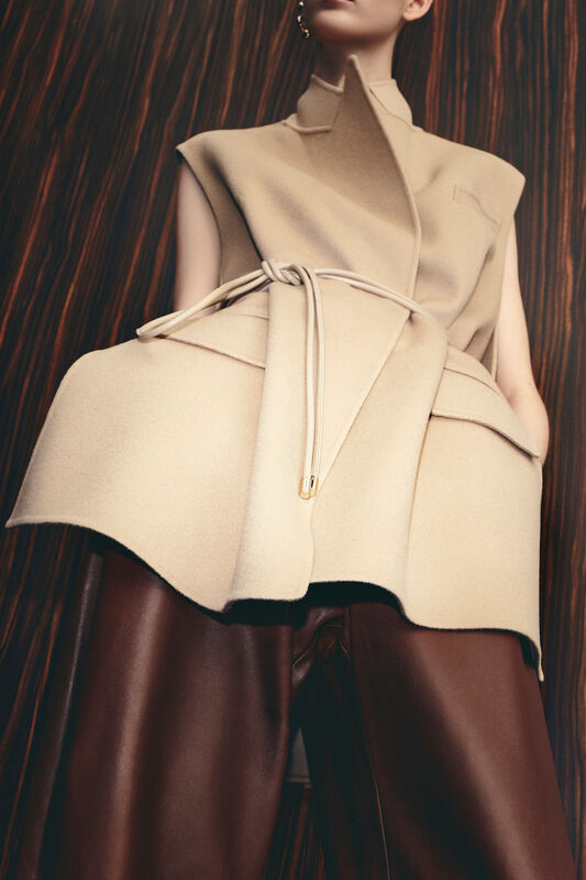 Элегантный бежевый жилет с асимметричным кроем и коричневыми кожаными брюками, создающими стильный силуэт