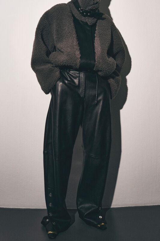 Модель в уютном сером жакете и кожаных брюках, подчеркивающих силуэт, с акцентом на детали кроя