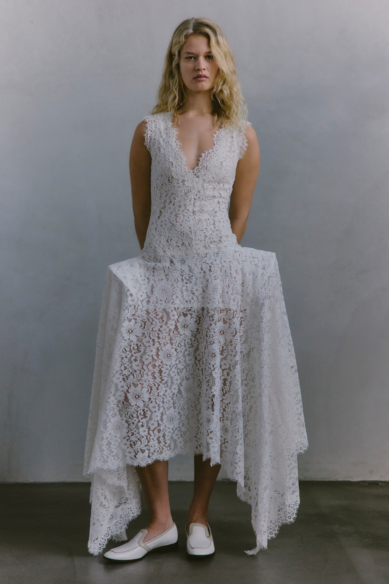 Нежное кружевное платье с асимметричным подолом и глубоким вырезом, завершенное белыми туфлями, излучает романтику.