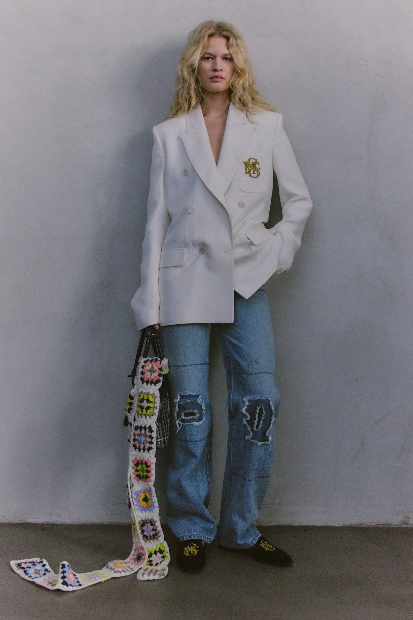 Белоснежный пиджак с логотипом и рваные джинсы создают стильный контраст в образе, дополненном яркой сумкой ручной работы