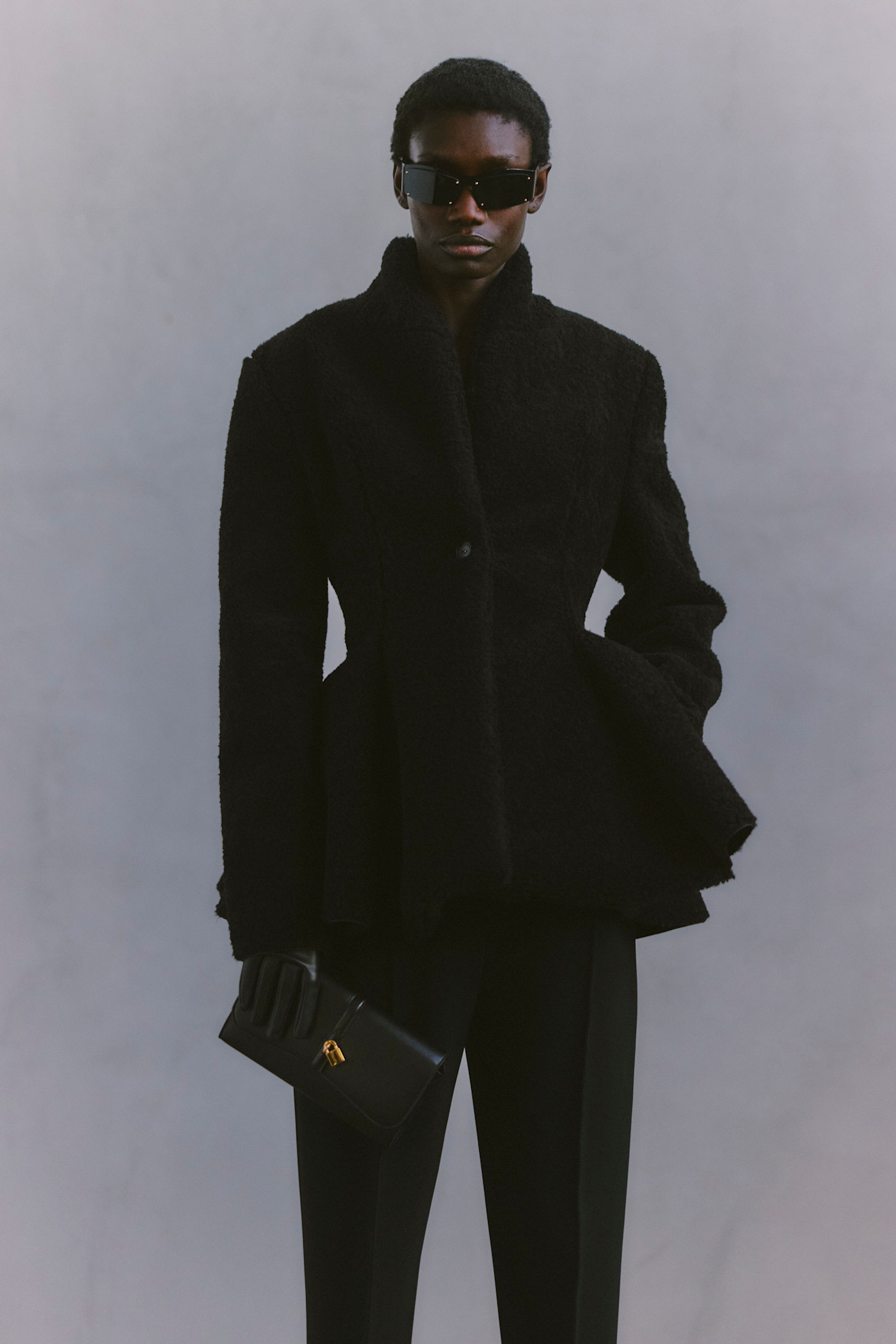 Черное пальто с текстурой и строгими линиями в сочетании с солнцезащитными очками формирует стильный и загадочный образ