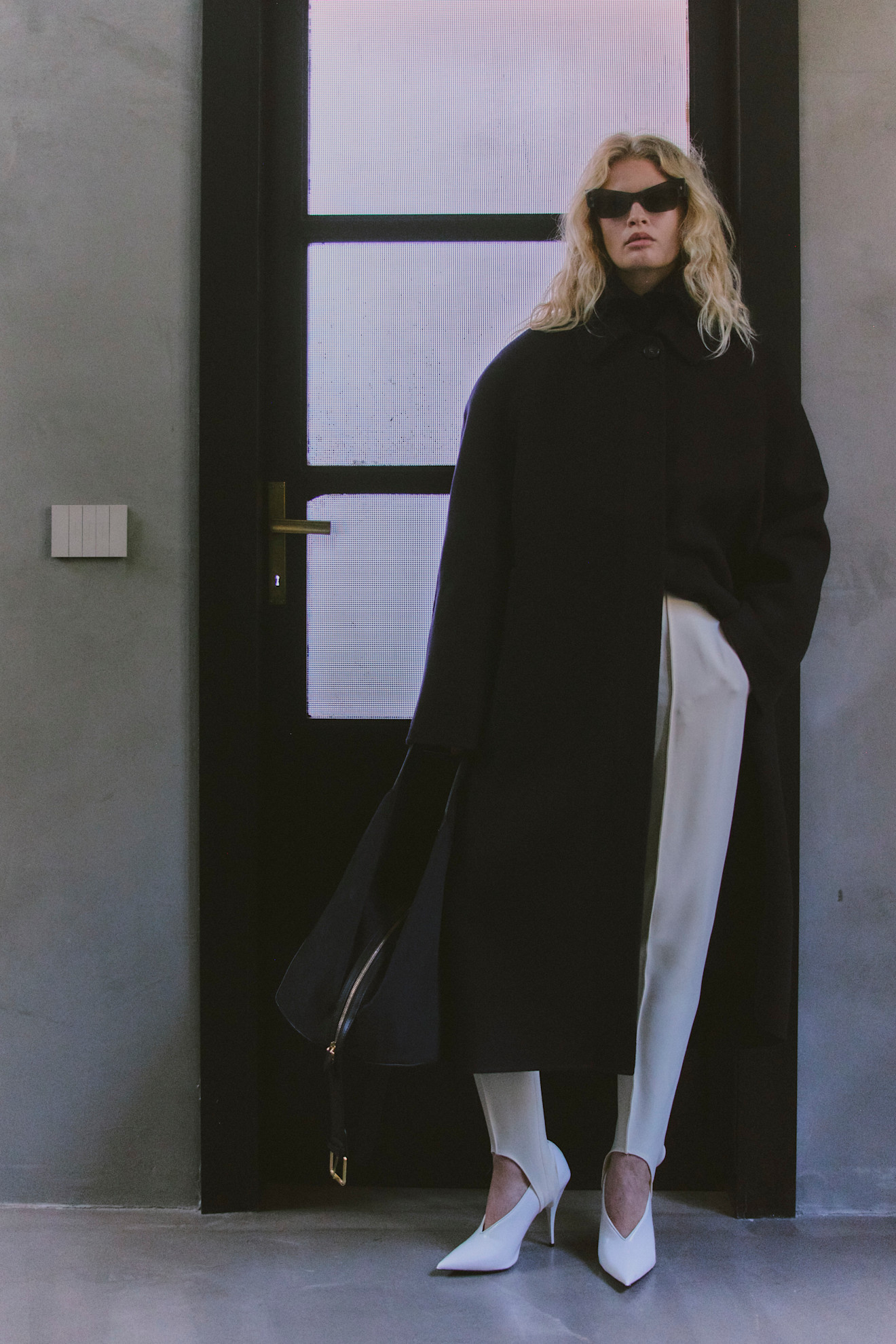 Стильный черный плащ, белые брюки и остроносые туфли, акцент на солнечных очках, минималистичный интерьер