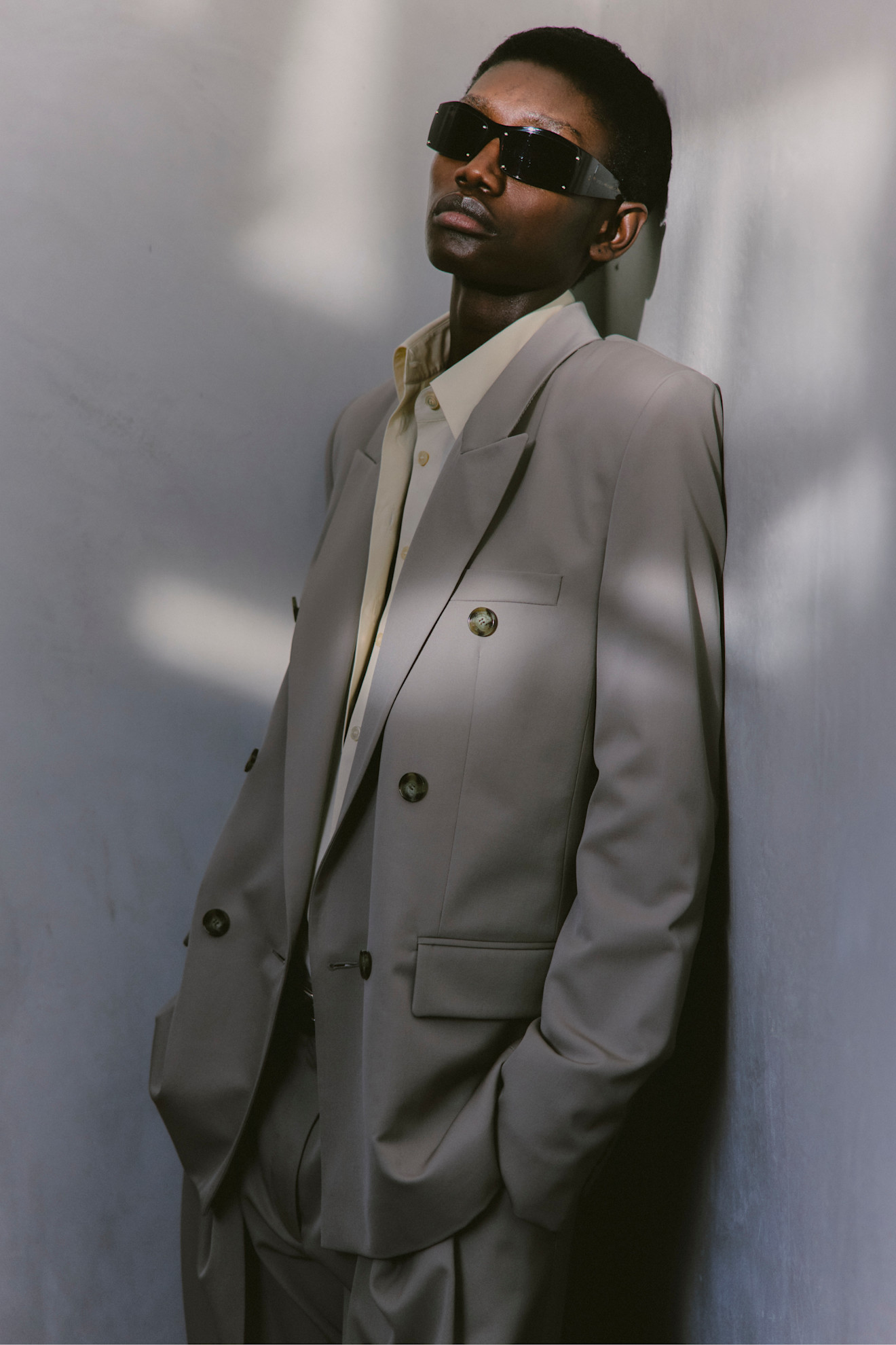 Стильный костюм светло-серого цвета с двойными пуговицами и черными солнцезащитными очками, подчеркивающий уверенность