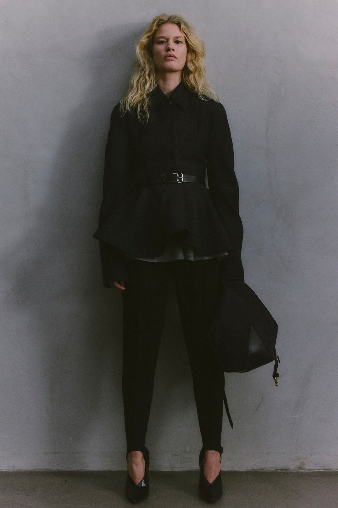 Элегантный черный жакет с пышным подолом и поясом, дополненный строгими брюками и стильной сумкой, подчеркивает силуэт модели