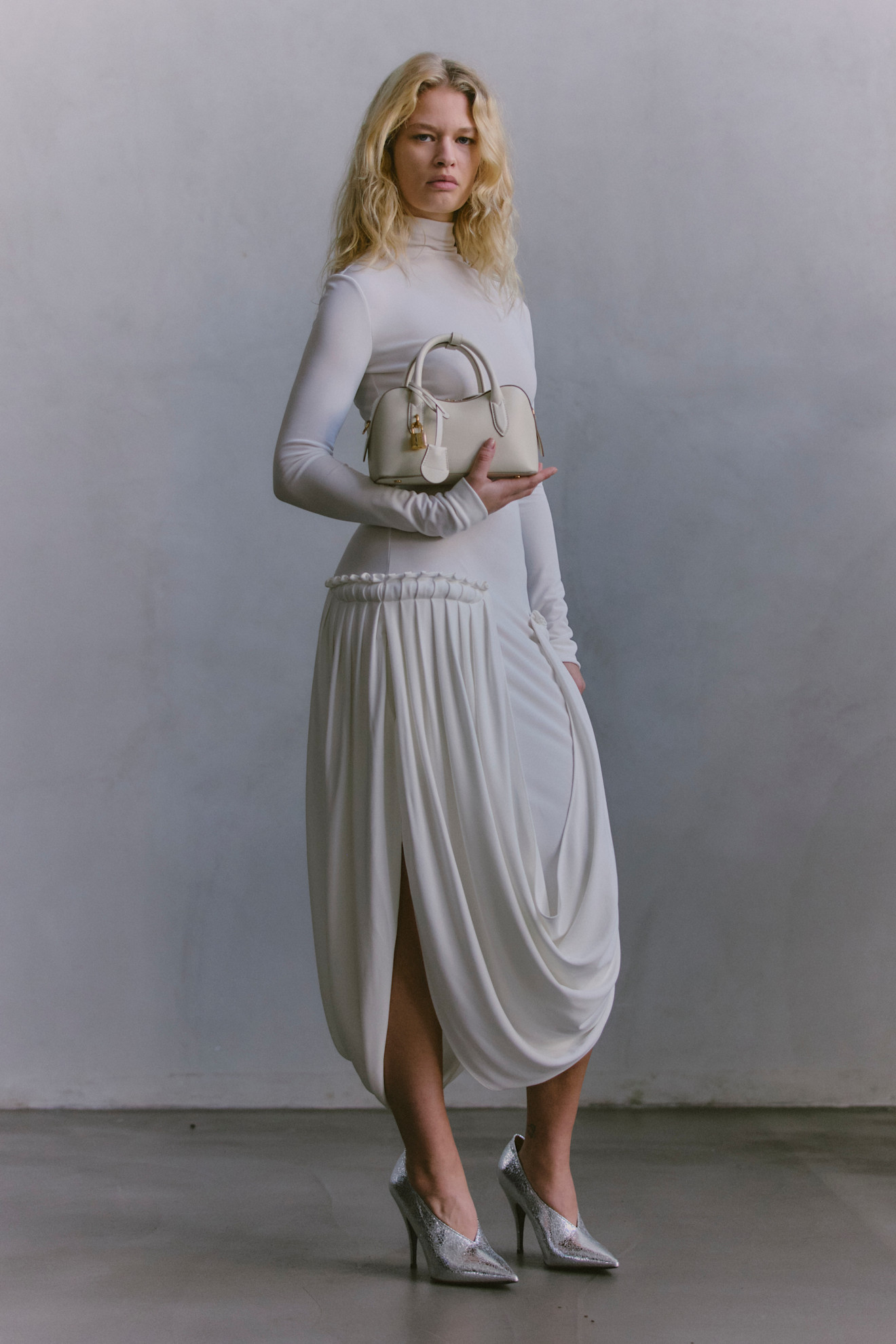 Элегантное белое платье с драпировкой и высоким разрезом, дополненное стильной сумкой