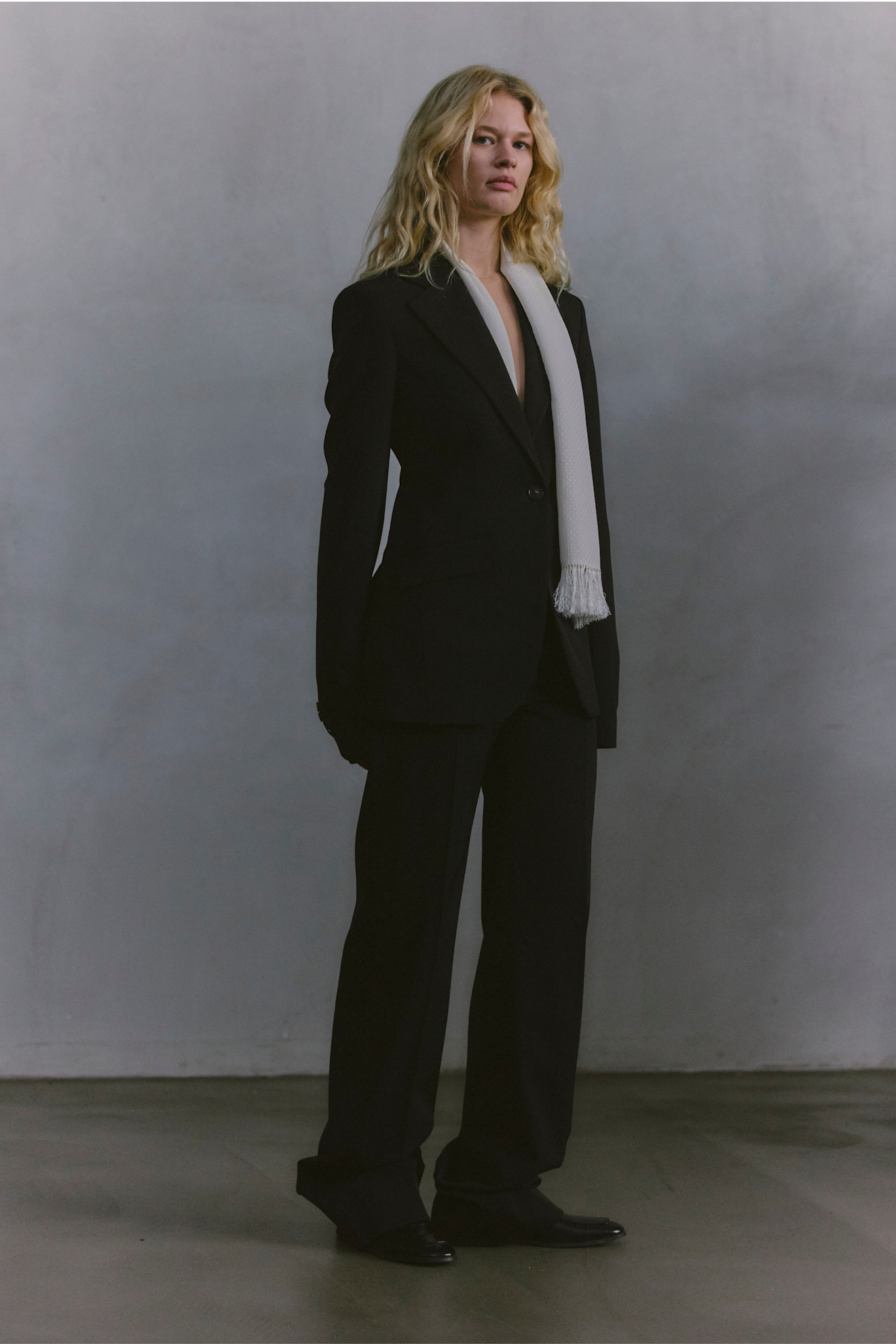 Строгий черный костюм с глубоким вырезом и светлым шарфом, создающий контраст, уверенный и современный образ