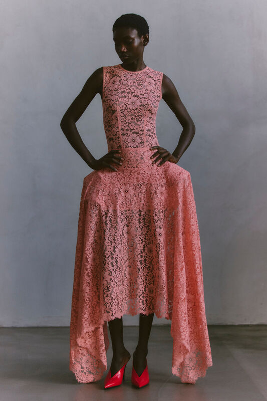 Яркое розовое кружевное платье с эффектом асимметрии и острыми красными туфлями, подчеркивающее силуэт.