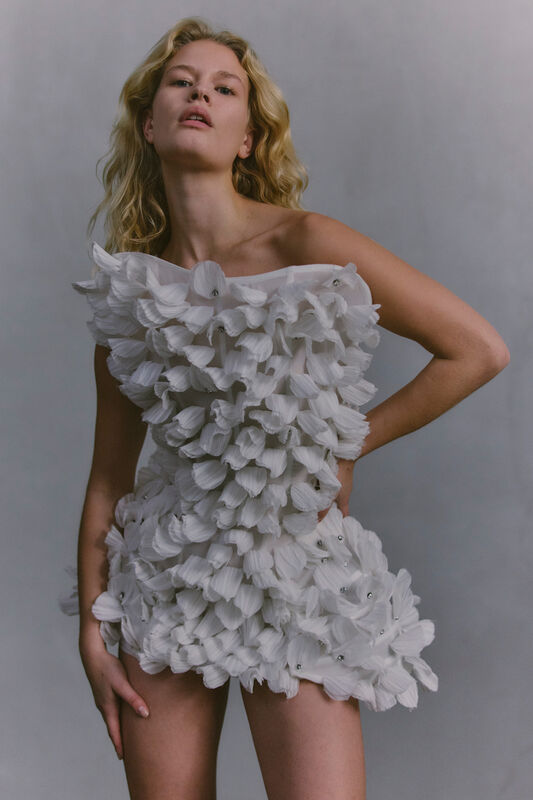 Мини-платье, украшенное объемными белыми лепестками, создает эффектный и игривый силуэт, привлекающий внимание