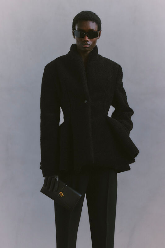 Черное пальто с текстурой и строгими линиями в сочетании с солнцезащитными очками формирует стильный и загадочный образ