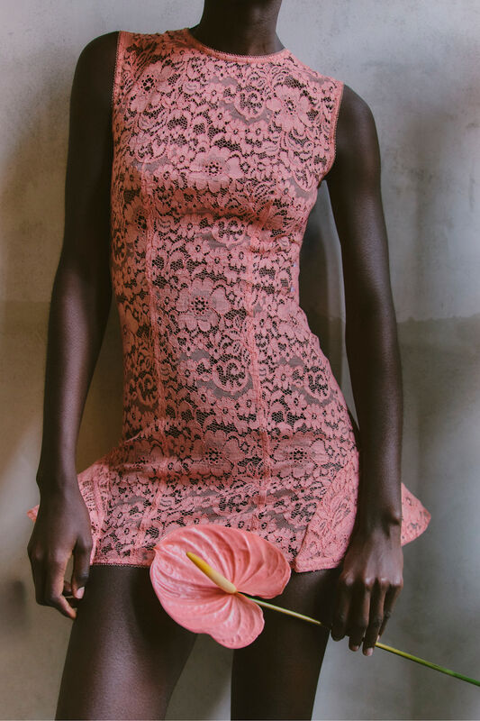 Нежное розовое платье из кружева с цветочным узором, подчеркивающее силуэт, в руках — яркий антуриум