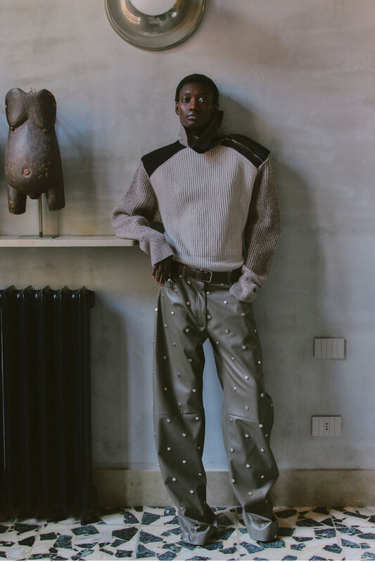 Модный свитер с текстурированными рукавами и кожаными брюками с металлическими элементами, создающими эффектный силуэт