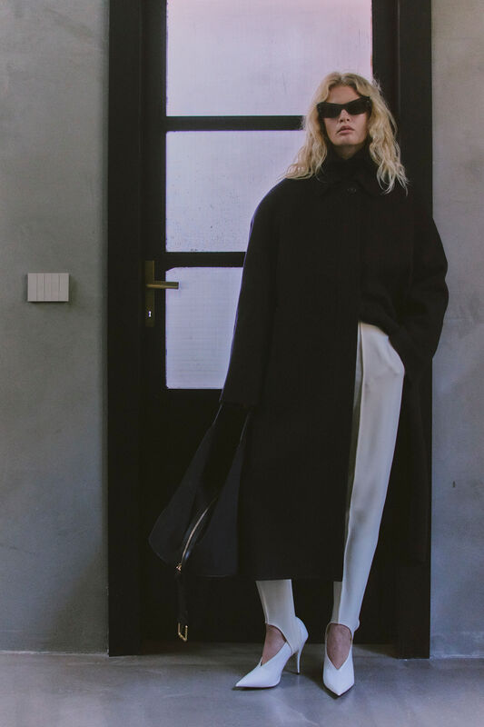 Стильный черный плащ, белые брюки и остроносые туфли, акцент на солнечных очках, минималистичный интерьер