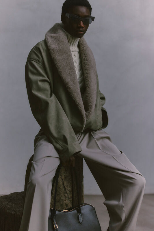 Уютный зеленый жакет с меховым воротником, вязаный свитер и светлые брюки, строгий стиль с черной сумкой в руках