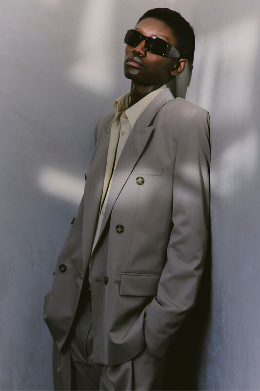 Стильный костюм светло-серого цвета с двойными пуговицами и черными солнцезащитными очками, подчеркивающий уверенность