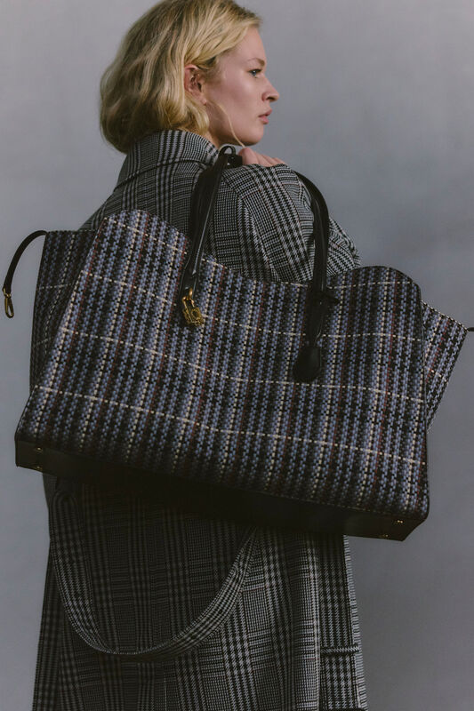 Женщина в клетчатом пальто с крупной сумкой в руках, демонстрирует утонченный стиль и внимание к деталям