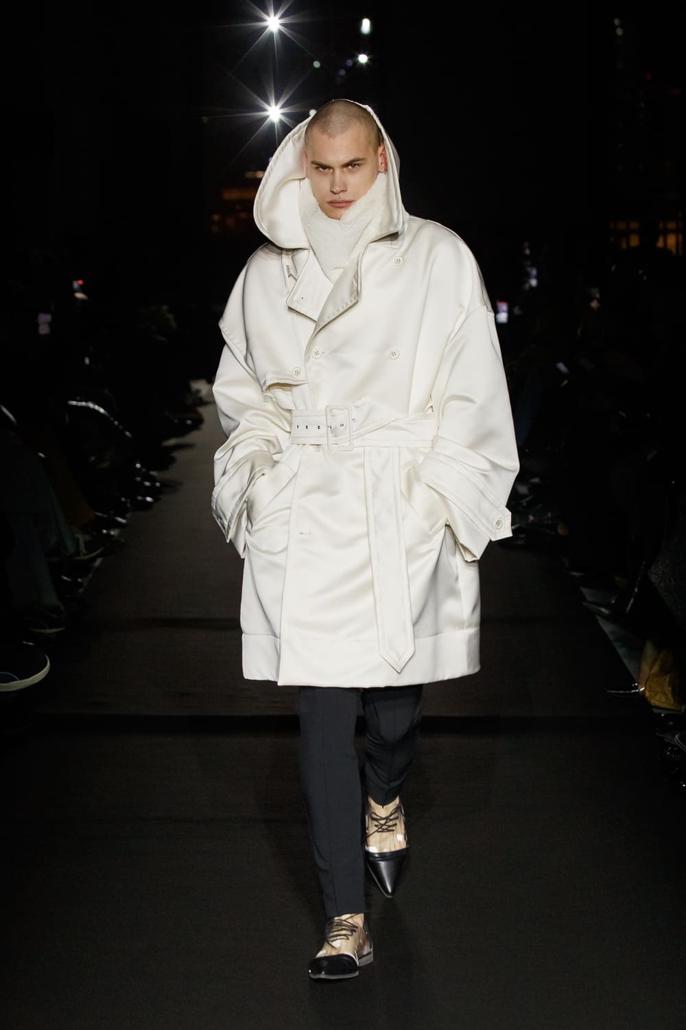 Модель в белом тренче с капюшоном и поясом, создающая эффектный контраст с черными брюками