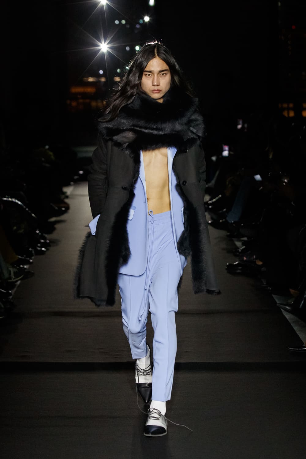 Модель в черном пальто с меховым воротником и светло-голубом костюме, подчеркивающая смелый стиль и уверенность