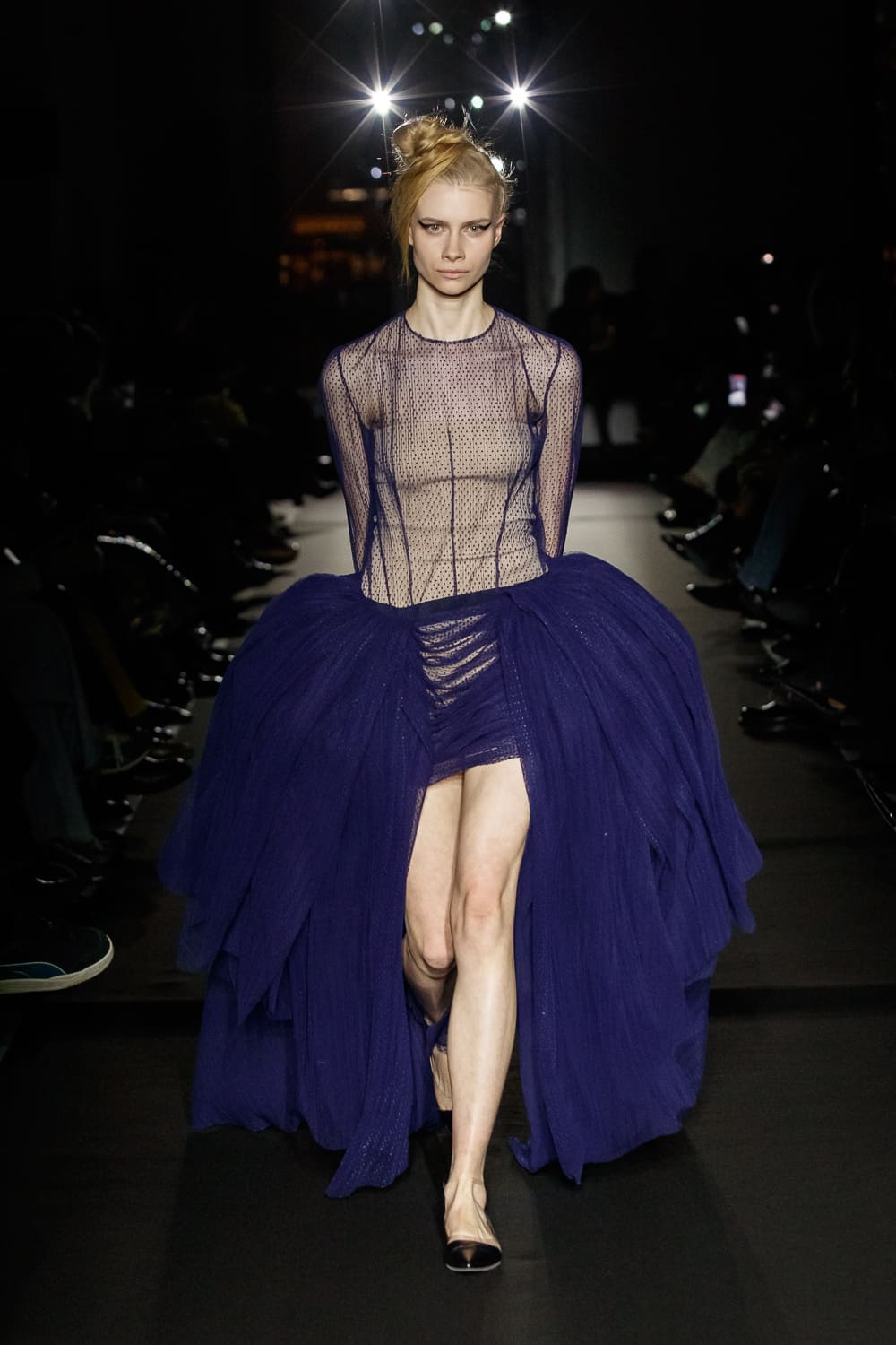 Полупрозрачное платье с объемной фиолетовой юбкой, создающее эффект легкости и загадочности на фоне темного зала