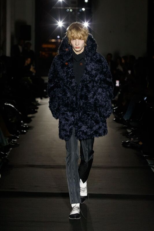 Модель в объемном темно-синем пальто и полосатых брюках, придающая образу неформальный шик