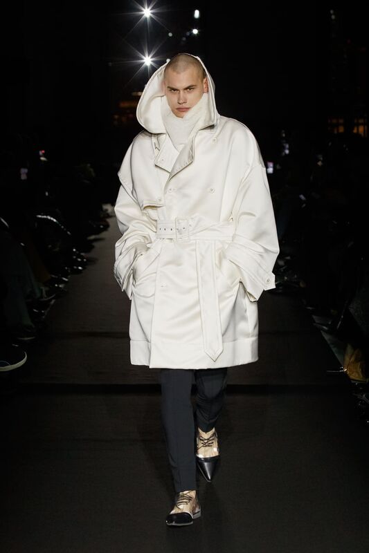 Модель в белом тренче с капюшоном и поясом, создающая эффектный контраст с черными брюками