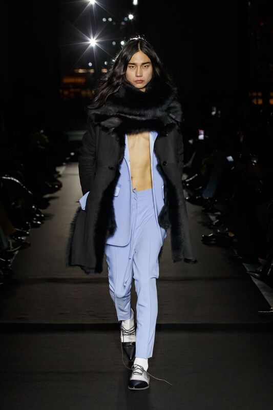 Модель в черном пальто с меховым воротником и светло-голубом костюме, подчеркивающая смелый стиль и уверенность