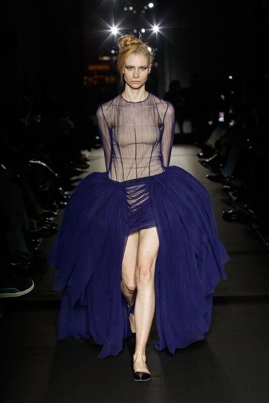 Полупрозрачное платье с объемной фиолетовой юбкой, создающее эффект легкости и загадочности на фоне темного зала