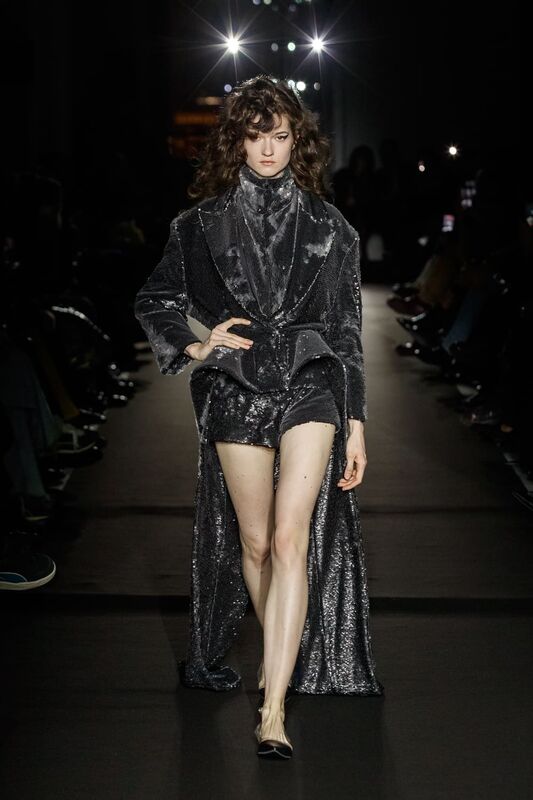 Блестящий наряд с короткими шортами и длинным пиджаком, создающий эффект вечернего сияния на подиуме
