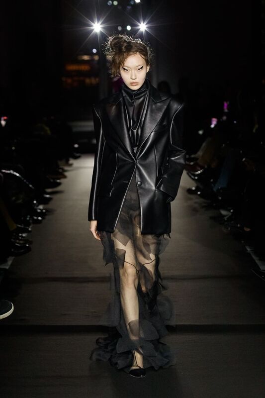 Образ в черном кожаном пиджаке с прозрачной юбкой, создающий эффект легкости и загадочности на подиуме