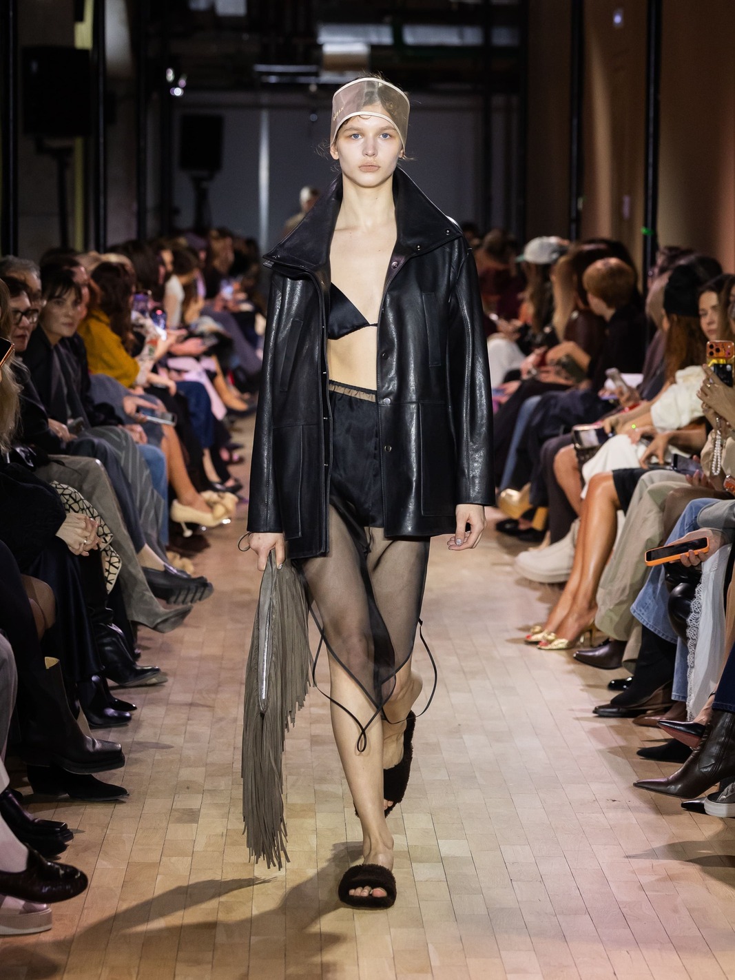 Кожаная куртка в сочетании с прозрачными шортами и аксессуарами из бахромы подчеркивает смелость и креативность дизайна.