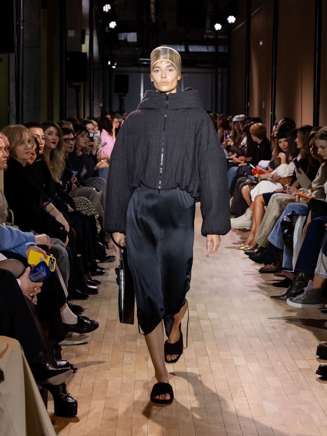 Объемная куртка в темном тоне и шелковое платье с разрезом, образ дополняет прозрачная шапочка и сандалии, подчеркивающие легкость стиля