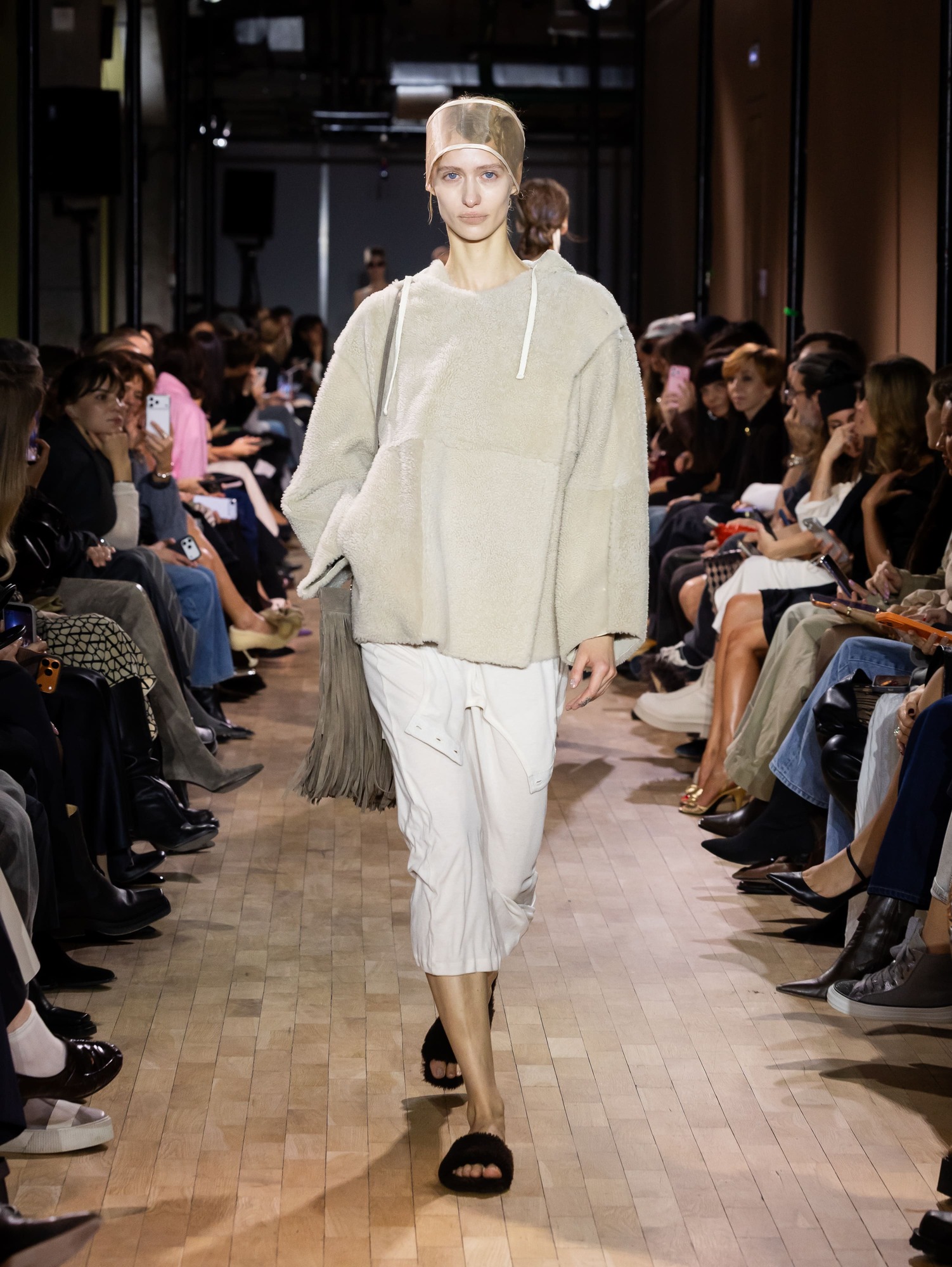 Объемный светло-бежевый свитер с капюшоном в сочетании с белыми брюками, создающий уютный и расслабленный образ