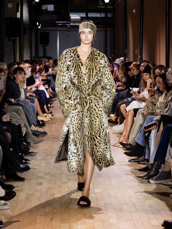 Модель в роскошном леопардовом пальто с поясом, сочетает элегантность и дикий шик, на фоне зрителей, погруженных в атмосферу показа
